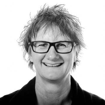 Person with short hair and glasses smiling against plain background